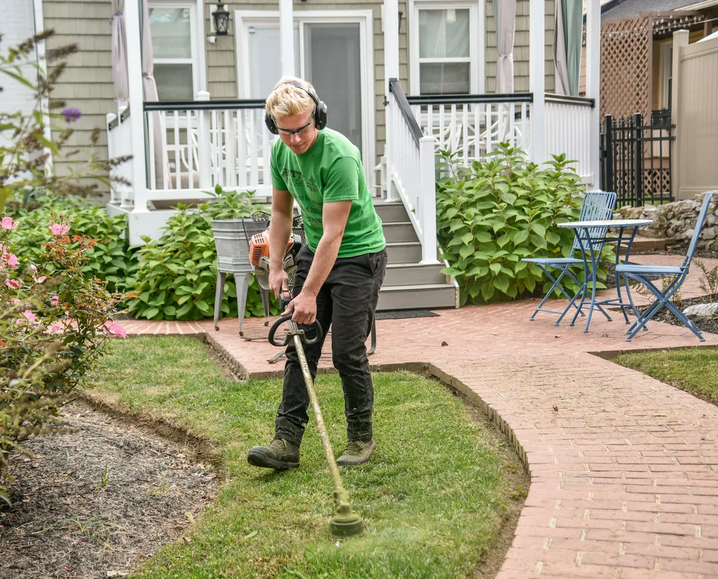An MC Landscaping crew member edging a lawn along a brick walkway
